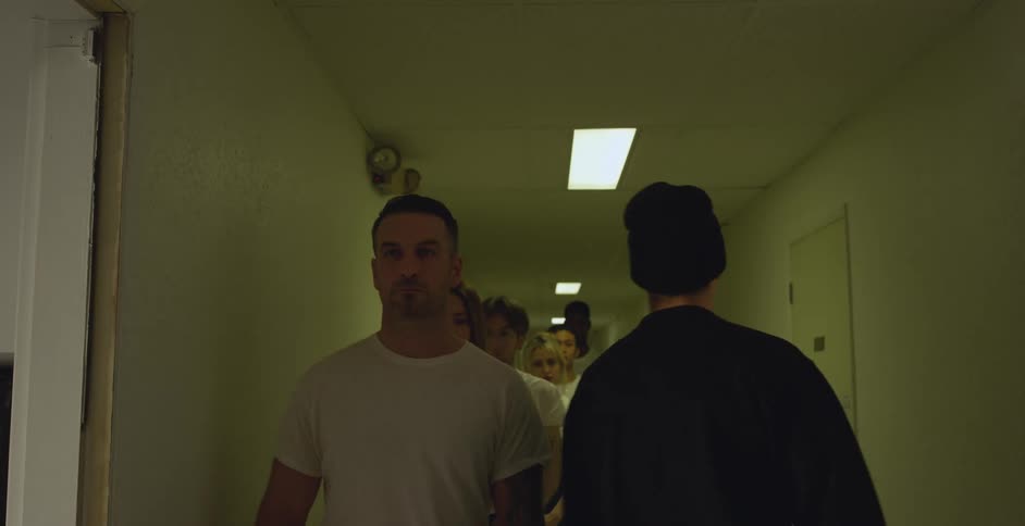 A group of young adults wearing white tshirts are lined up in a corridor