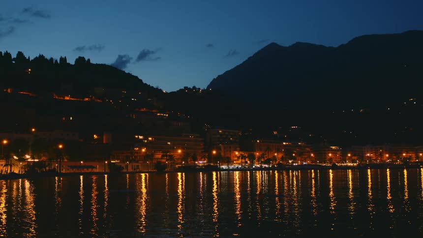 Residential area by a lake at night with residential lighting on the horizon a mountain range