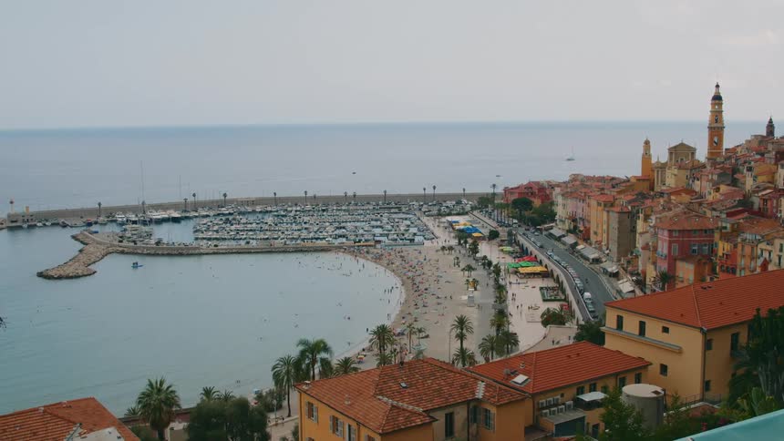 Aerial view of a suburb with old residential properties along the shore of a beach with bathers and yachts