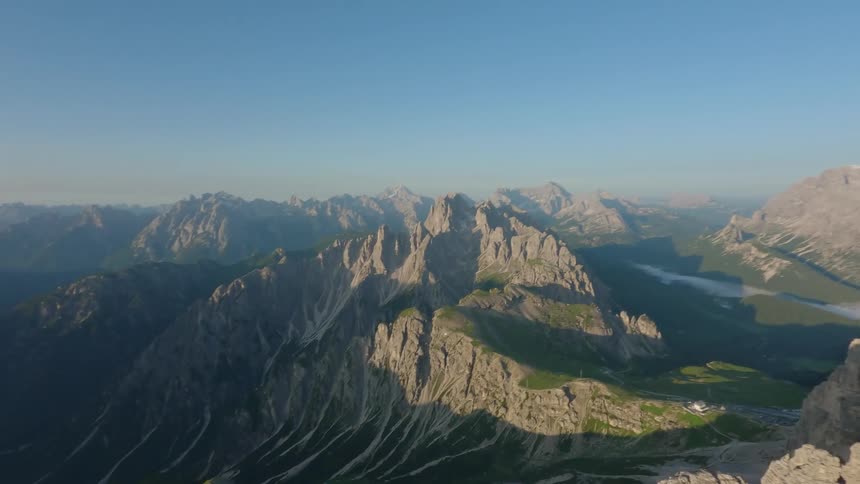 Drone view of tall rock faces with mountain ranges in the lower elevation on a bright sunny day