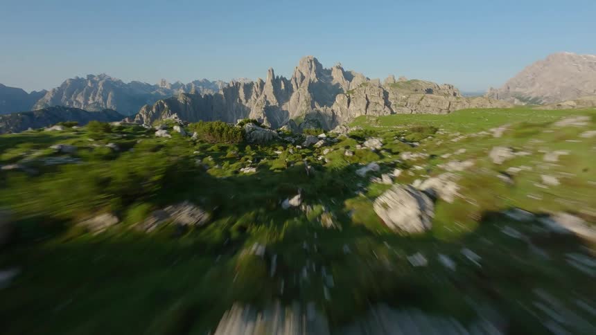 Dolomites FPV zooming fast low close Rocks scattered across the grass with mountains and rock formations in the distance