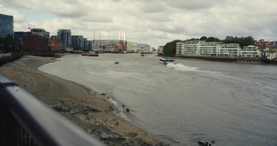 Boat sailing down the River Thames towards Battersea on a cloudy as the waves crash against the embankment