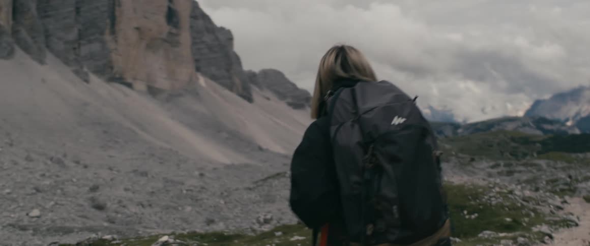Woman with a backpack and hiking attire observing the rocky nature on a mountain