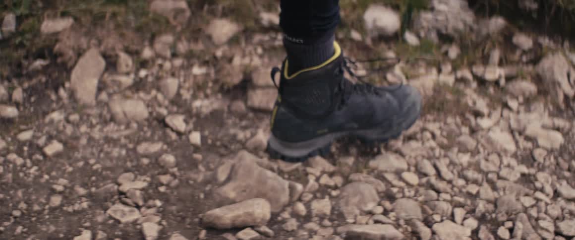 A person wearing black boots is walking on a stone and rock covered trail