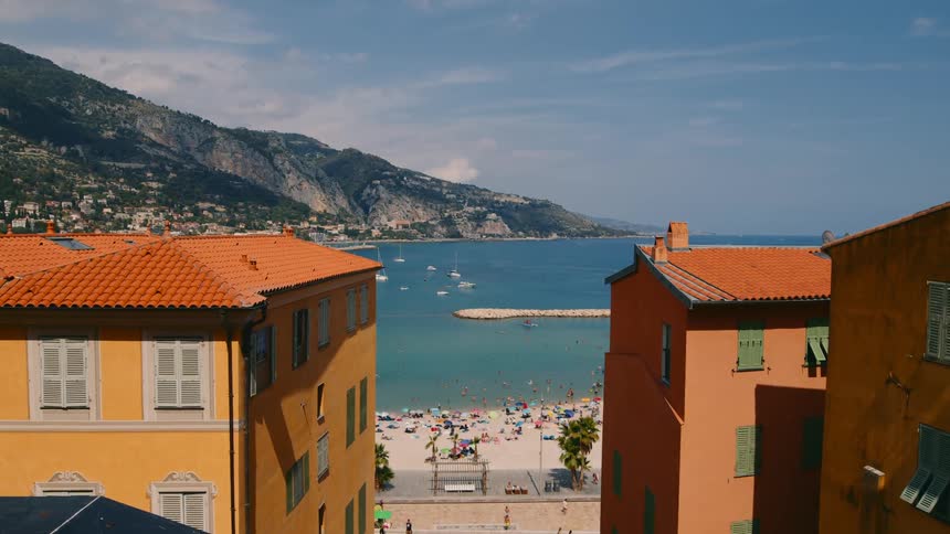 View of a beach on a summer day with several people and old residential buildings around and in the background the coastal shoreline
