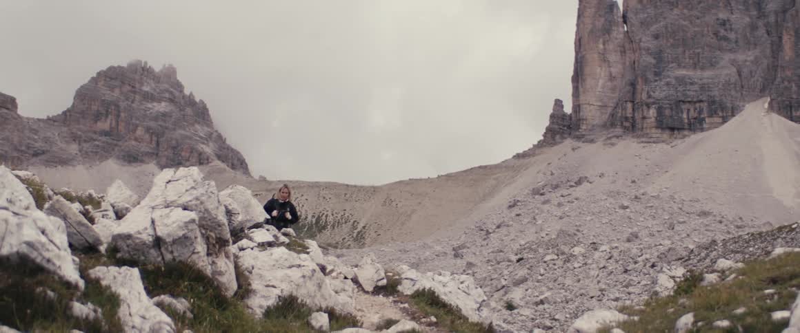 A woman walks in a deserted landscape with mountains