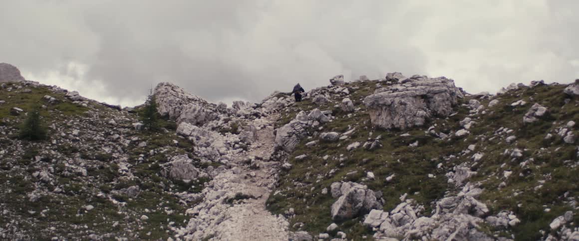 A hiker is walking up a rock covered mountainside under a cloudy sky
