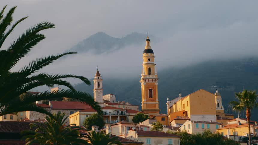 A tower stands prominently above a town located near a towering mountain