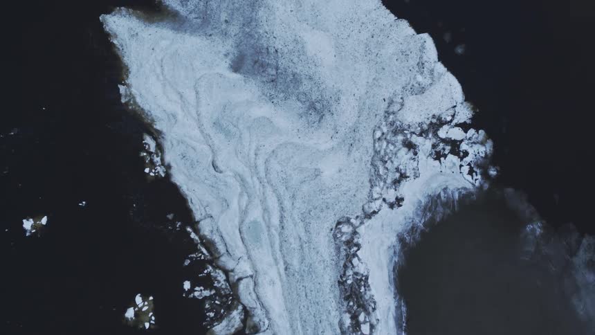 Ice formations are scattered in the water by a rock formation