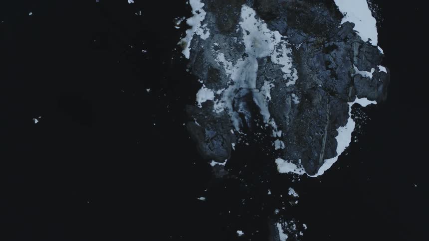 Ice formations are scattered in the water by a rock formation