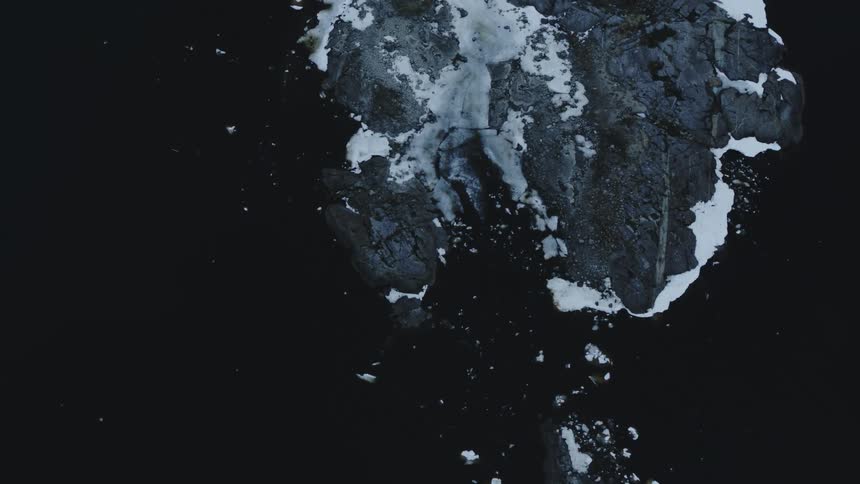 Birds fly near a snow-covered rock outcropping surrounded by icebergs
