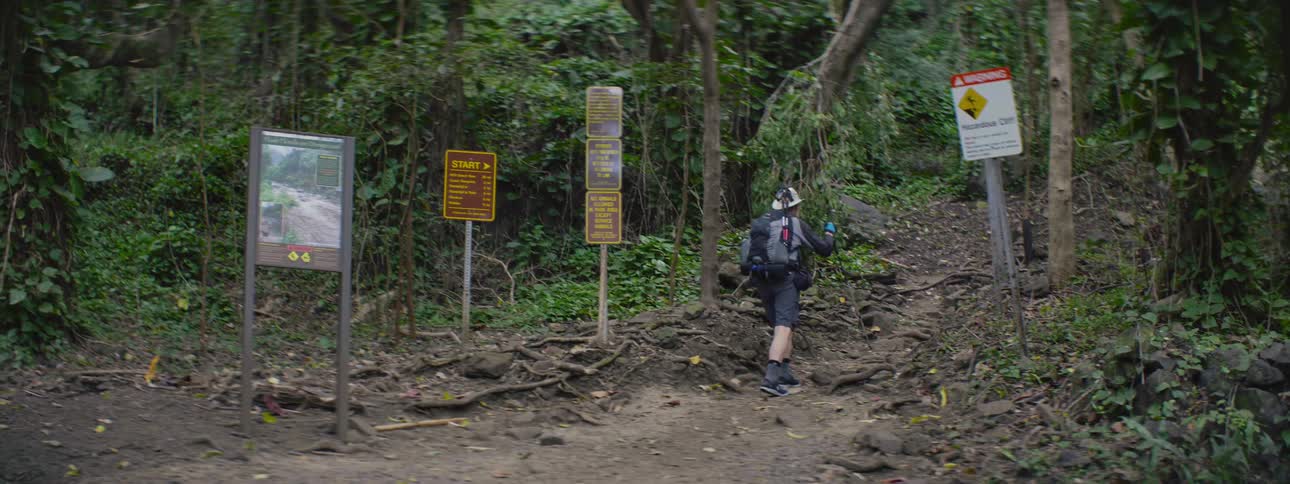 A man is hiking up a trail past several informational signs