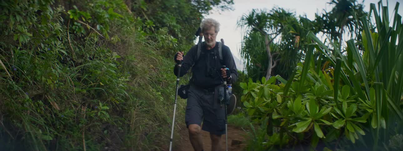 An older man is hiking on a trail in a tropical area
