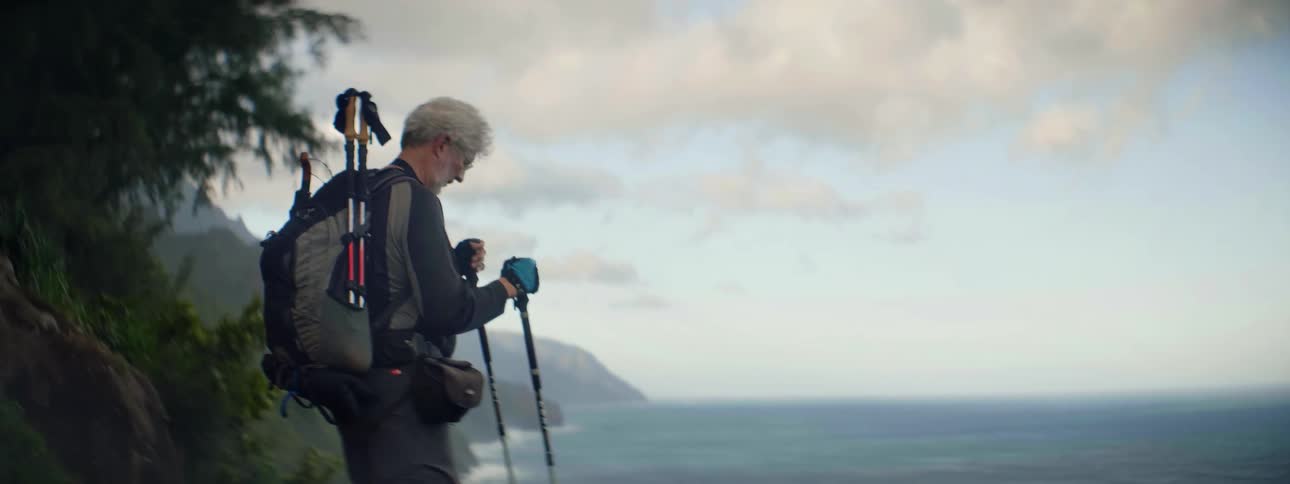 Man carrying walking sticks looks out at the ocean
