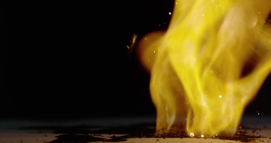 Yellow flames rise from burning surface releasing sparks into the dark