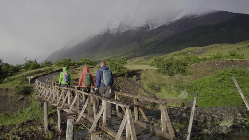 Hikers walk across a small wood bridge in the mountains
