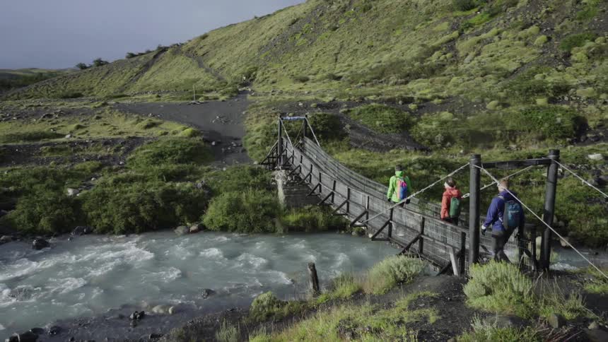 Hikers cross over a river on a wood bridge