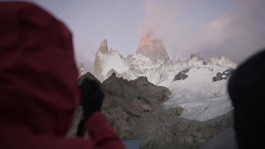 A hiker takes a photo of a snowy mountain peak