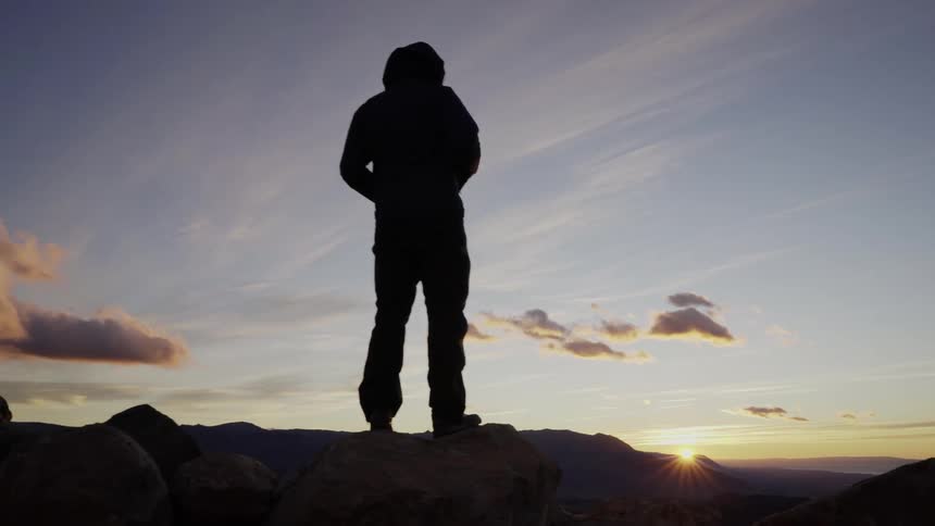 A man stands on the rocks at sunset