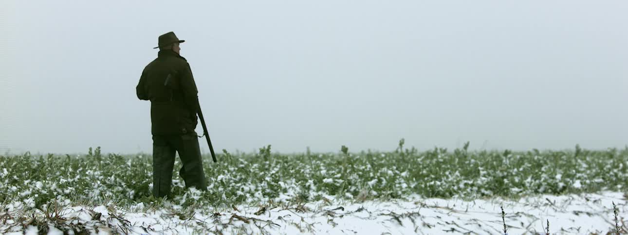 A man standing in a field holds a rifle