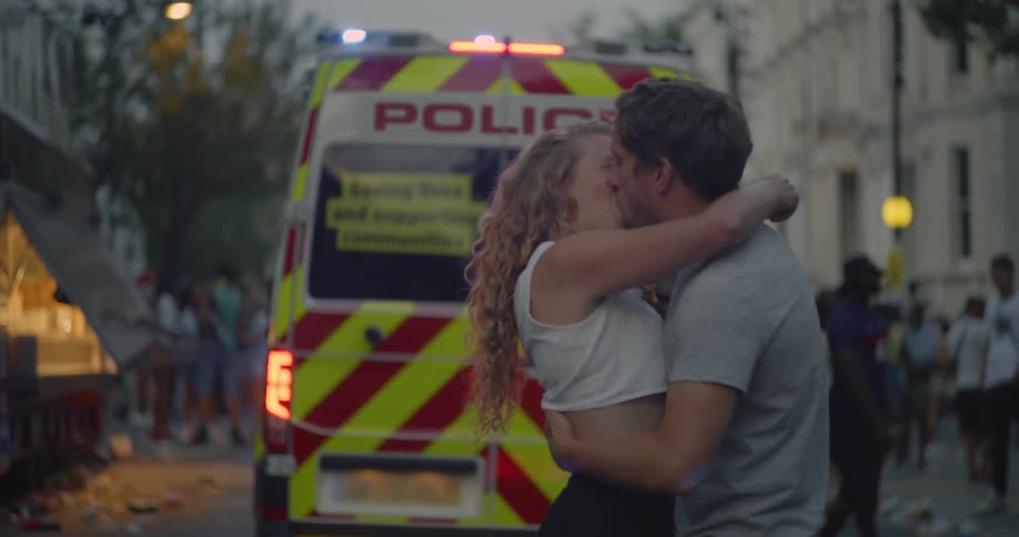 Man and woman kiss and embrace in front of police van as it pulls away