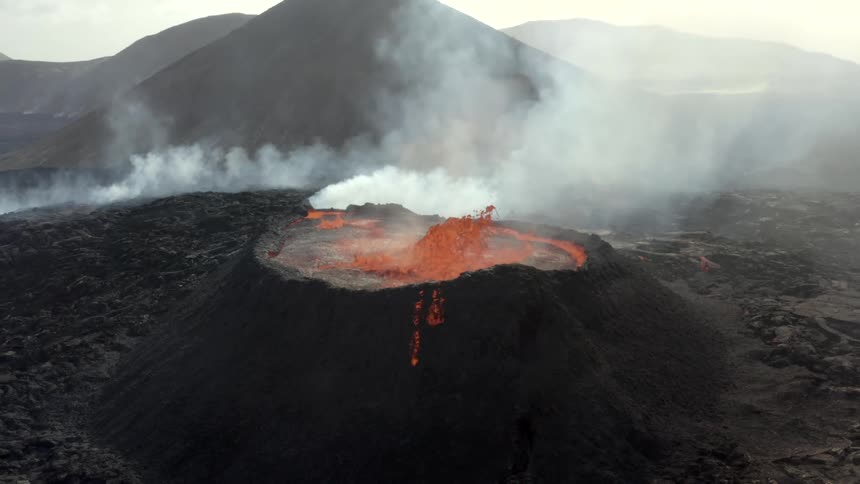 Molten hot lava splashes into the air as an active volcano erupts and smoke rises
