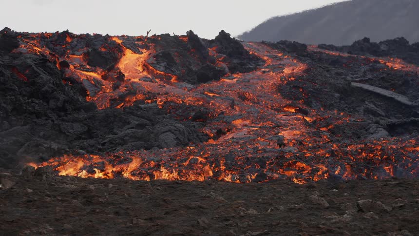 A volcano erupts as flaming hot glowing magma flows down the side
