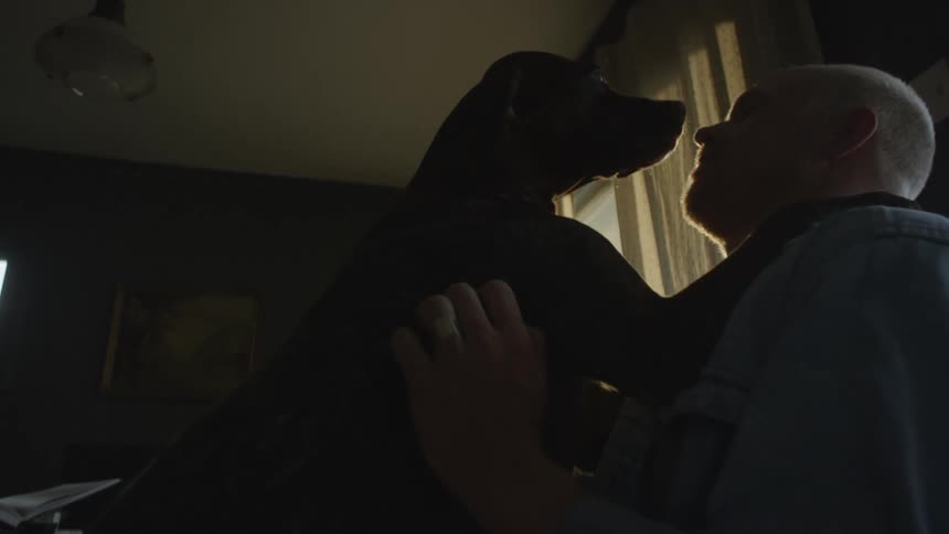 Whitehaired man indoors petting his dog as it licks his face