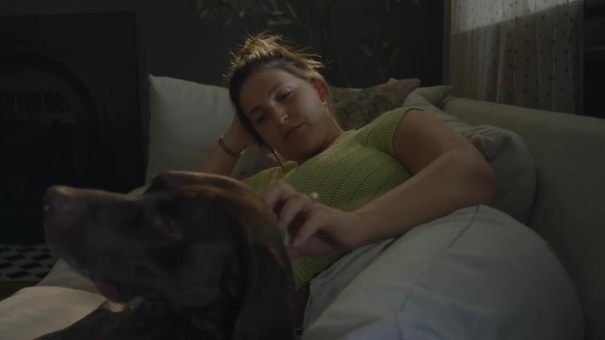 Woman lays on couch and pets dog