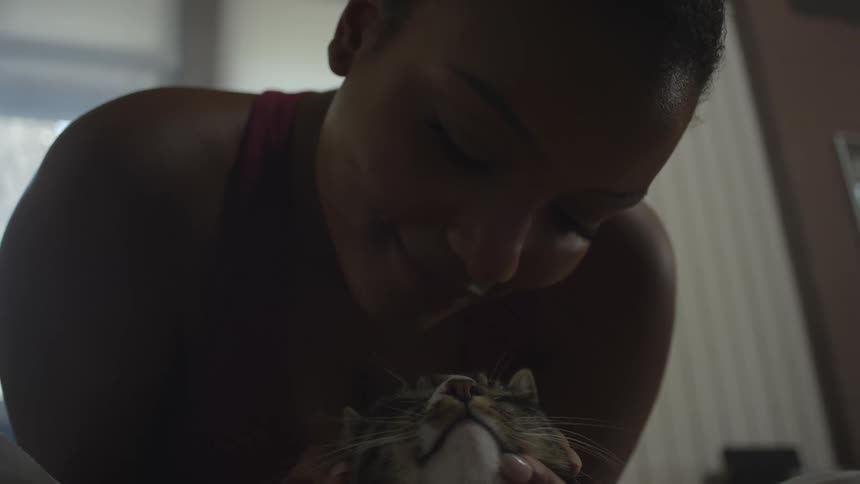 A girl smiles as she pets her cat with both hands and kisses it