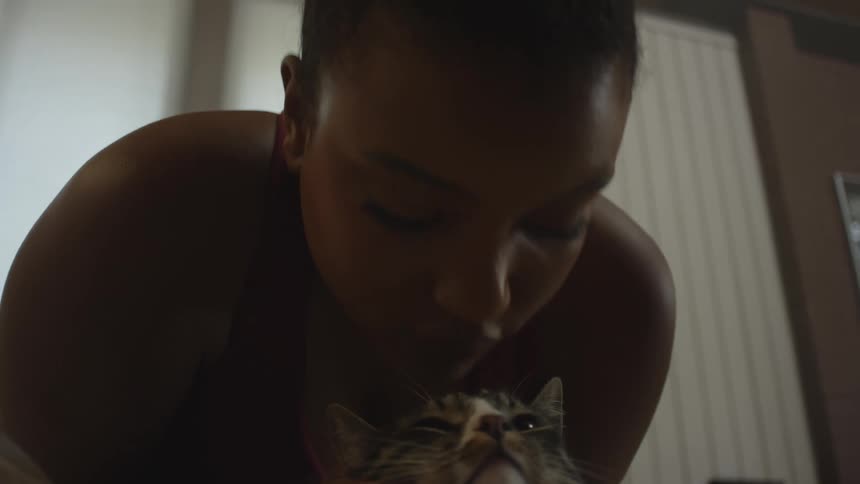 Black woman standing up kissing and fondling a cat indoors during day time