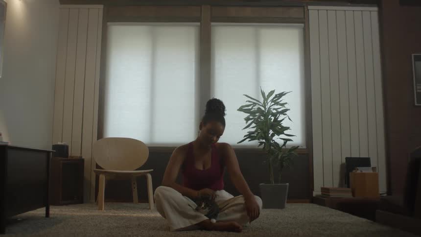 Woman sits cross legged on floor while petting cat on lap