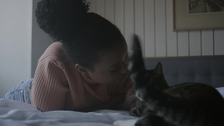 Black woman indoors laying down and petting a cat during day time