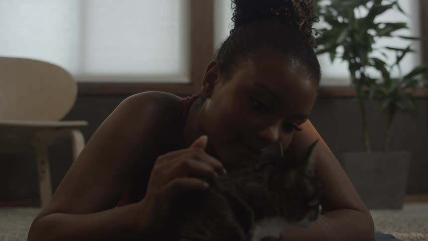 A woman is petting a cat lying on the floor