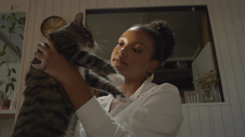 A teenage girl holds her cat in the air and gives it a kiss and then holds it close with a big hug
