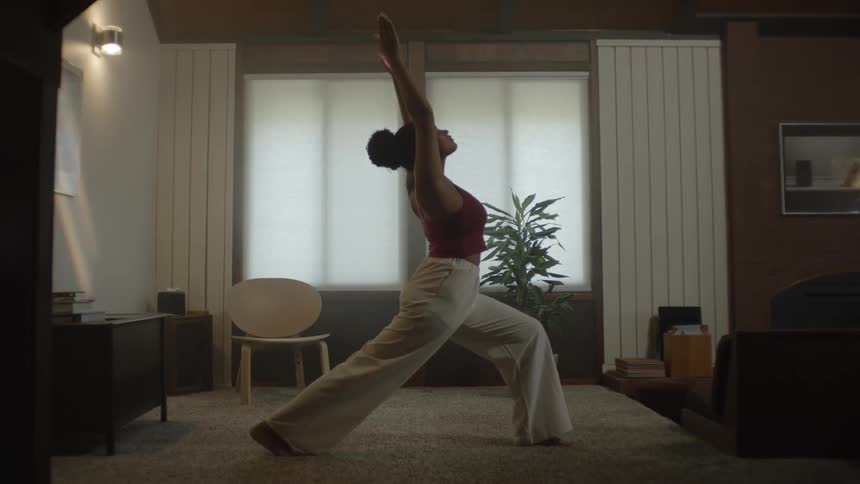 Oung black woman exercising her body standing in yoga poses within a living room