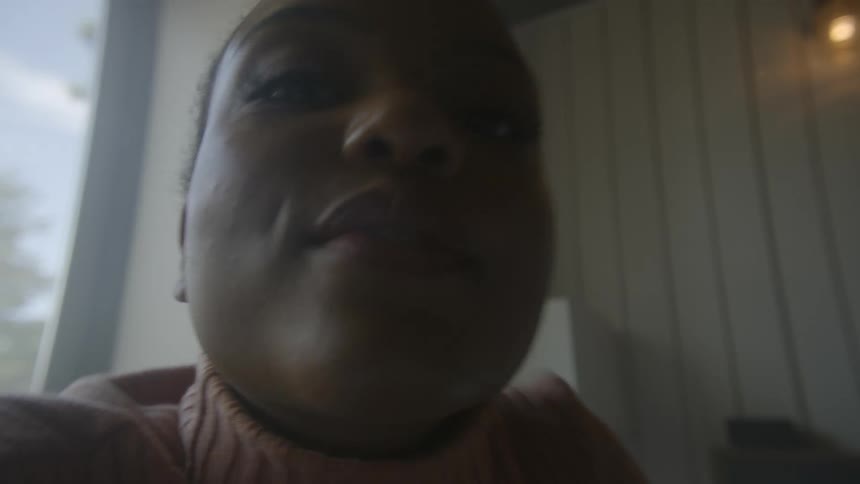 Black woman caressing and kissing something outside the frame indoors during day time