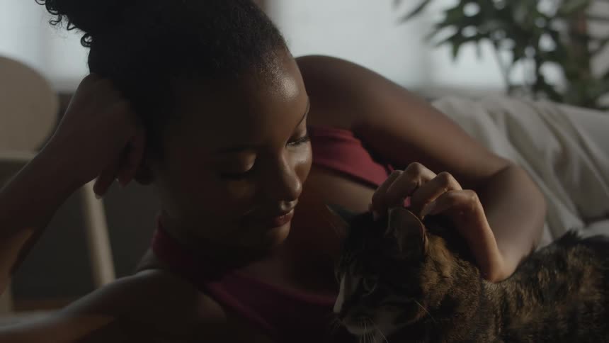 Young black woman lying down giving a kiss and affectionately petting her pet cat