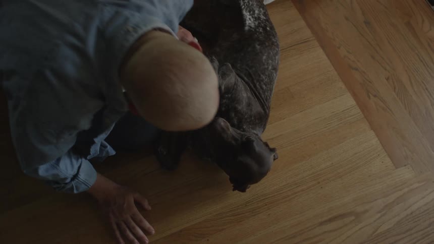 Bald man indoors playing with a black dog during day time