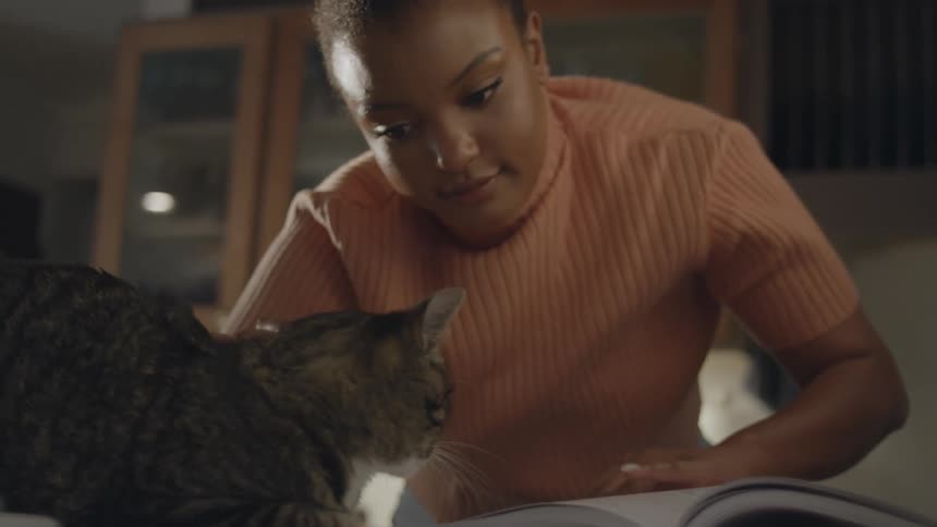A woman pets and kisses a cat while reading a book