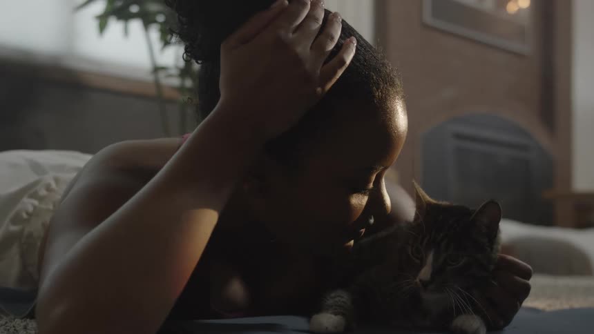 Woman lying on her stomach pets and cuddles her cat