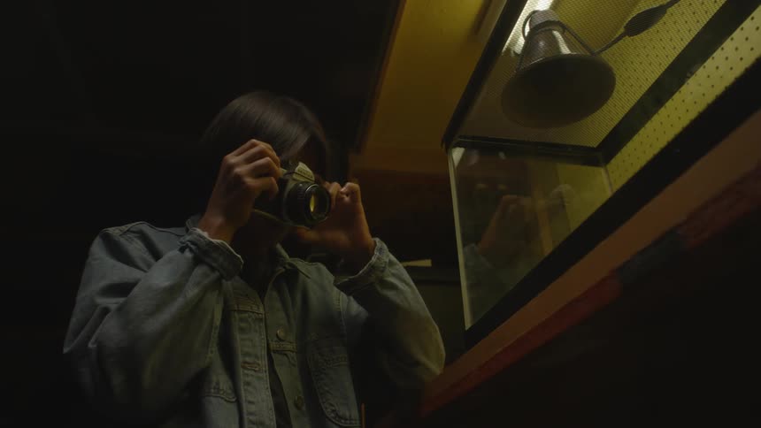 Woman photographing an enclosed environment through glass with low lighting