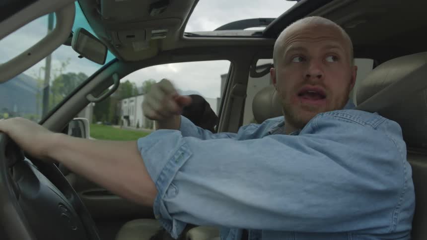 Bald man driving a car through the streets with a dog on the passenger seat during day time