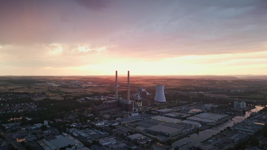 Aerial view of a power plant within a city with the sunset in the background on the horizon
