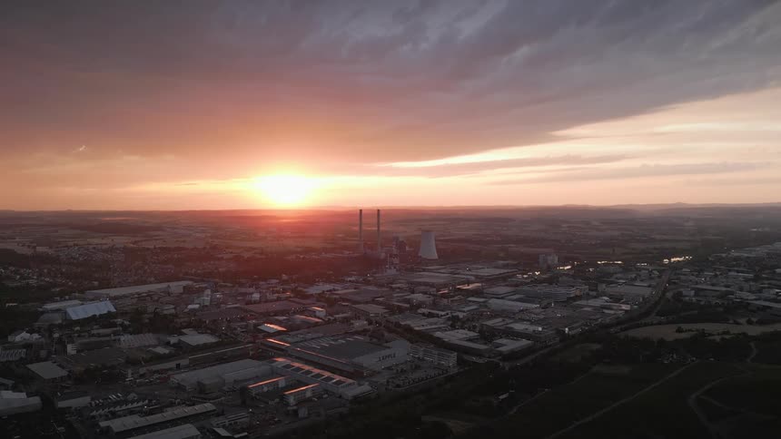 Automobiles travel on roads by buildings and parking lots near a nuclear plant as the rising sun shines brightly on the horizon