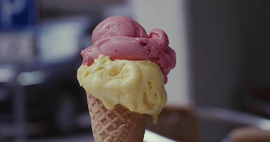 An ice cream with yellow and pink flavours melting