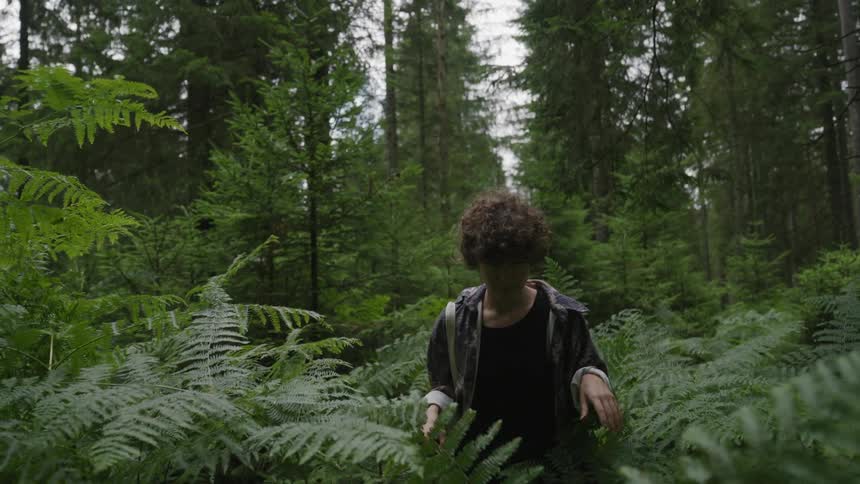A young person walking through plants in the middle of a dense forest