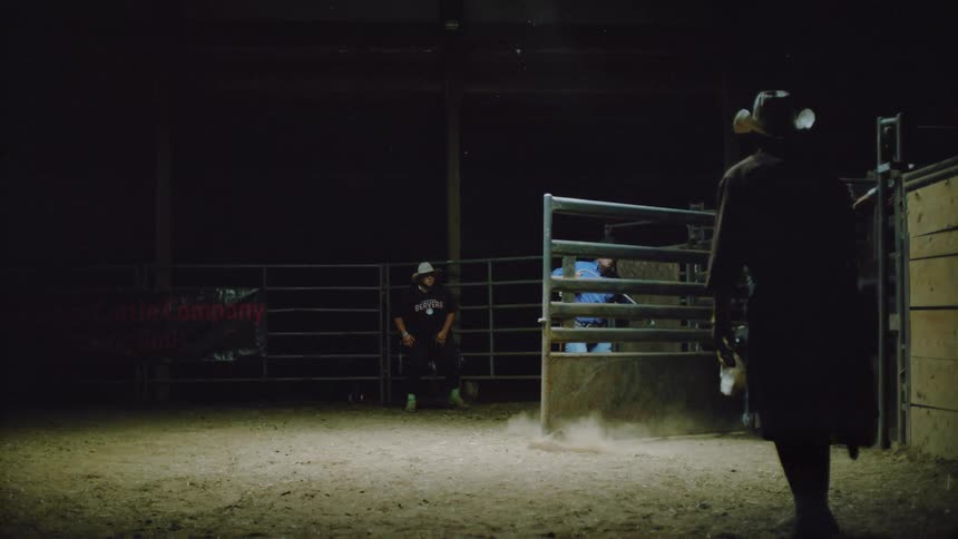 Several men stand in a rodeo ring and one lets a bull out of its pen