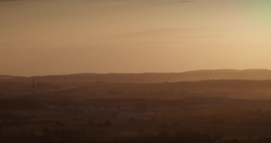 A field with hills on the horizon and in the background the light of the rising sun at dawn