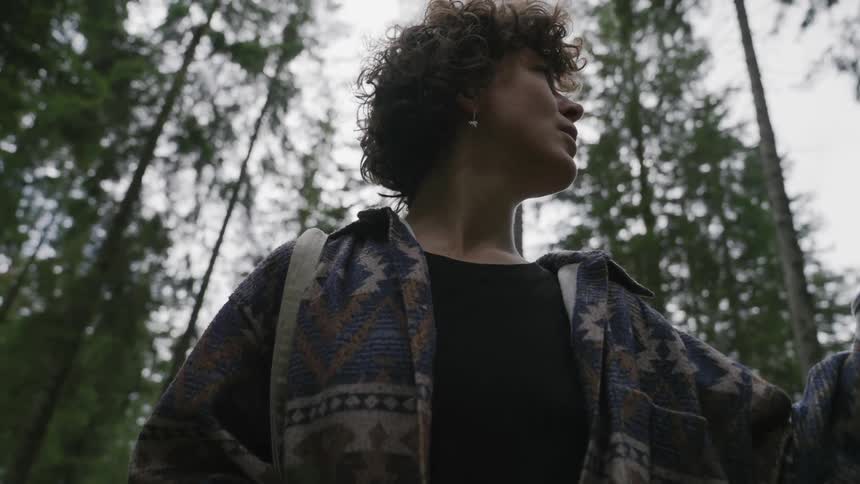 Woman in a coat in the midst of a forest pointing to a specific location